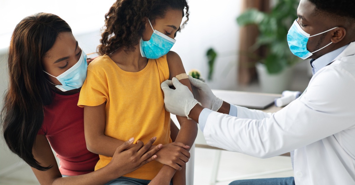 Pediatrician placing medical band on a little girls shoulder with her mother