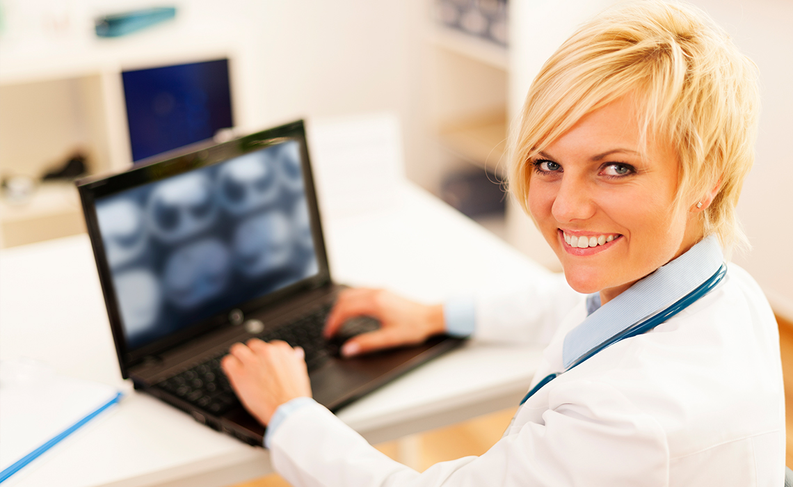 A smiling radiologist in front of a computer showing mammography results