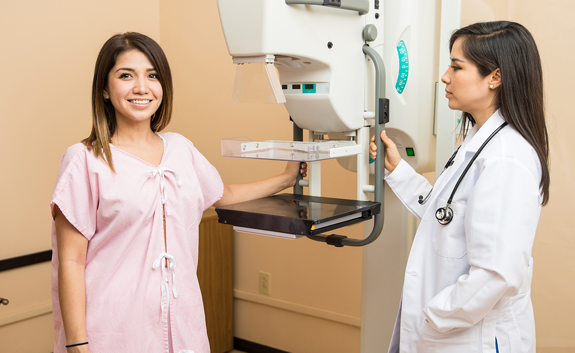 A patient standing by a radiologist and a mammography machine